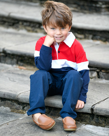 young boy in a red and blue color block polo sitting on stairs