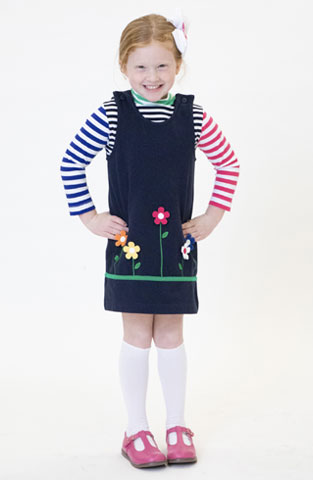 young girl in navy jumper with flower appliqué and multi-color striped long sleeve shirt
