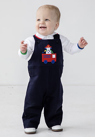 toddler boy standing up in a navy firetruck longall and white long sleeve shirt