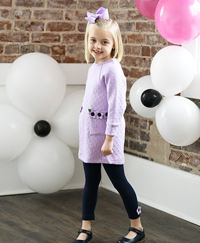 young girl in a purple long sleeve jumper with purple flowers on the pockets and matching leggings